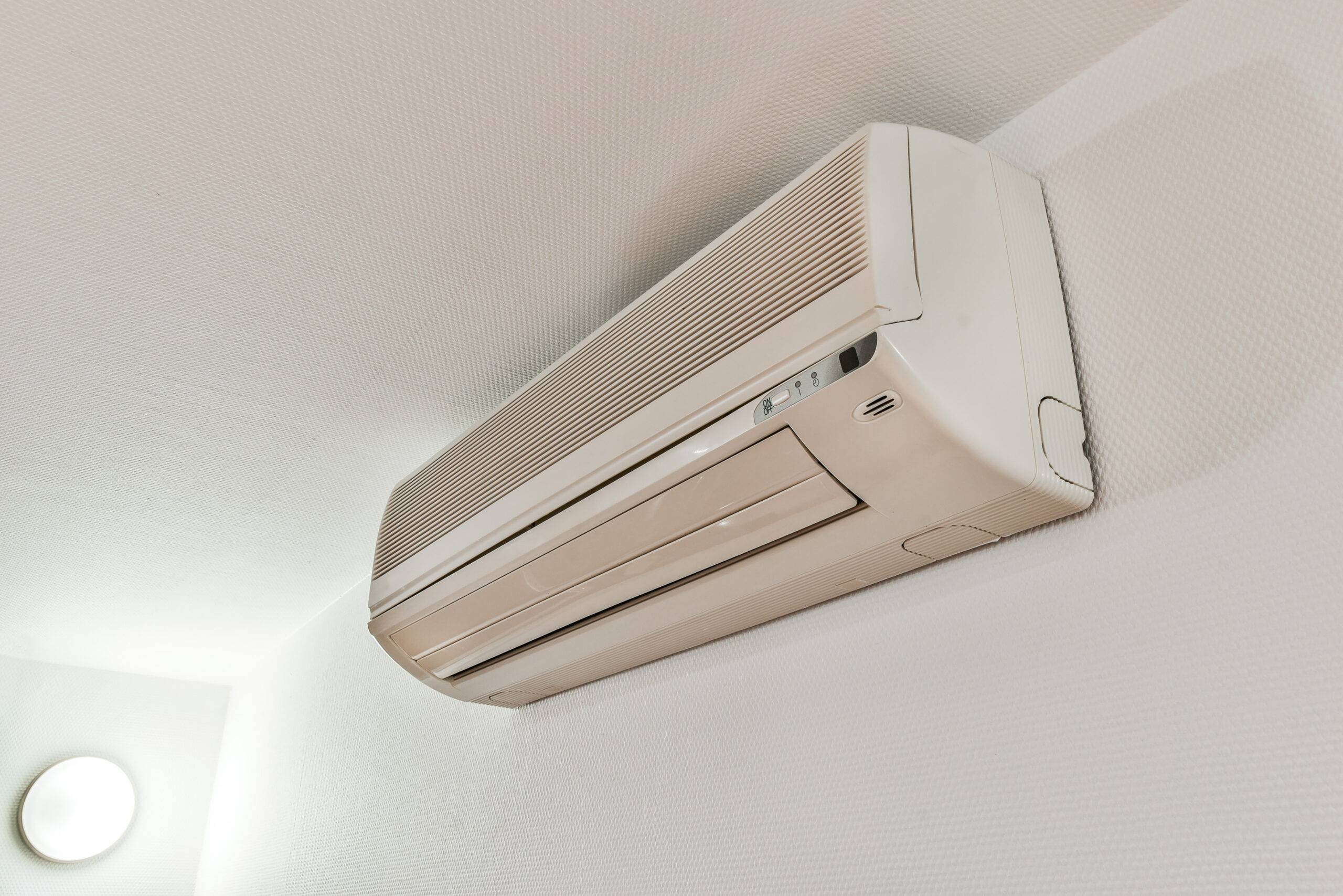 From below modern air conditioner hanging on white wall under ceiling in room