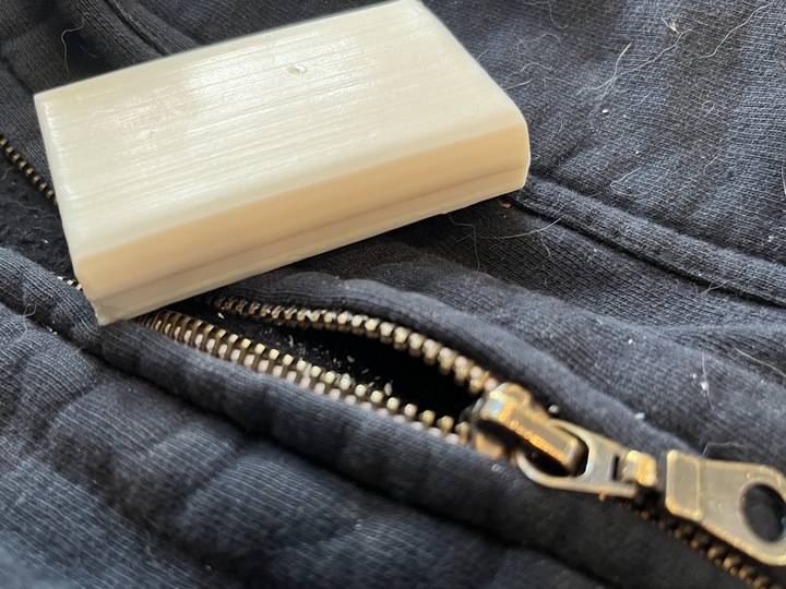 A close photo of a bar of soap laying atop a sweater zipper.