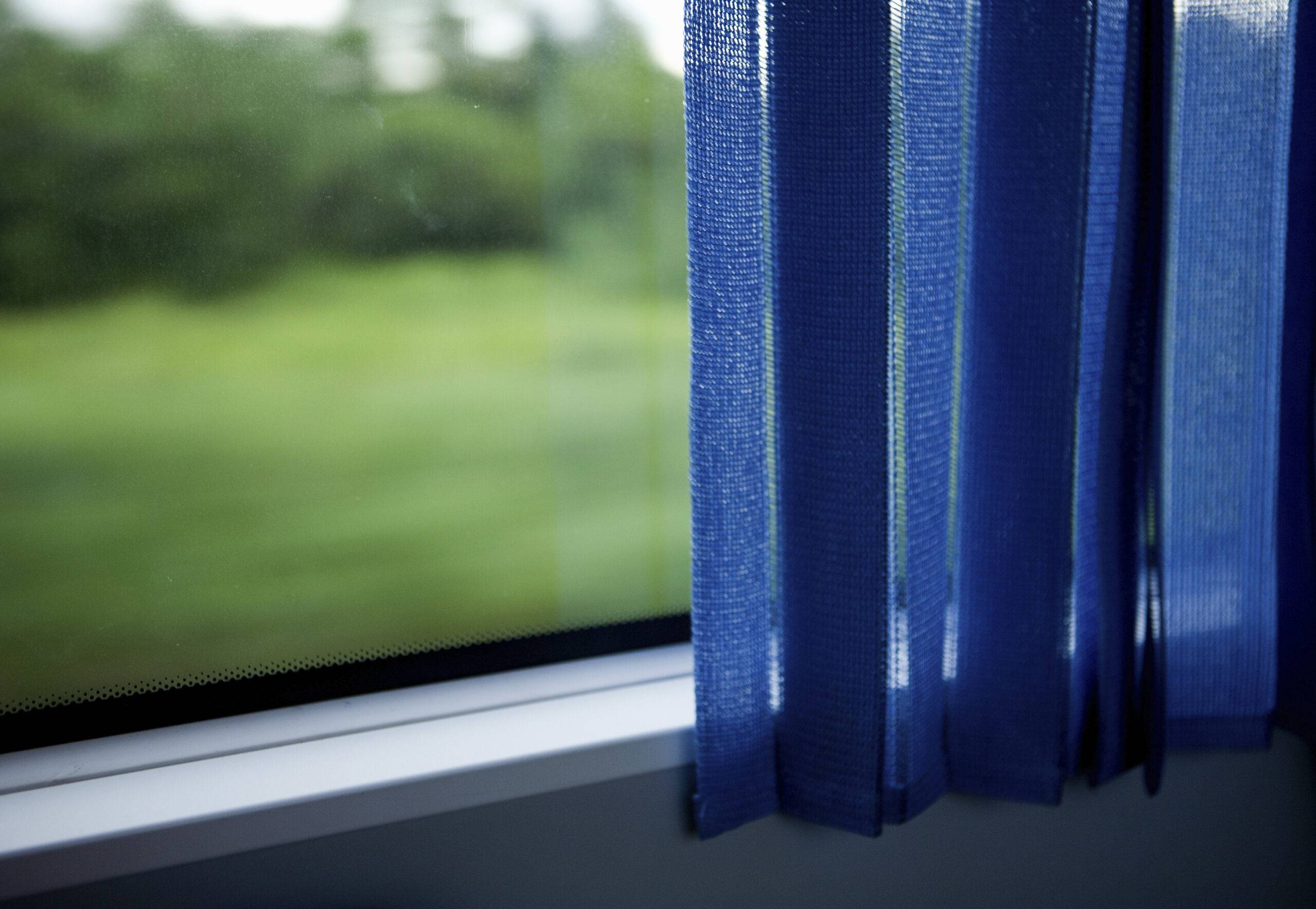 A window with a blue curtain half pulled over it.