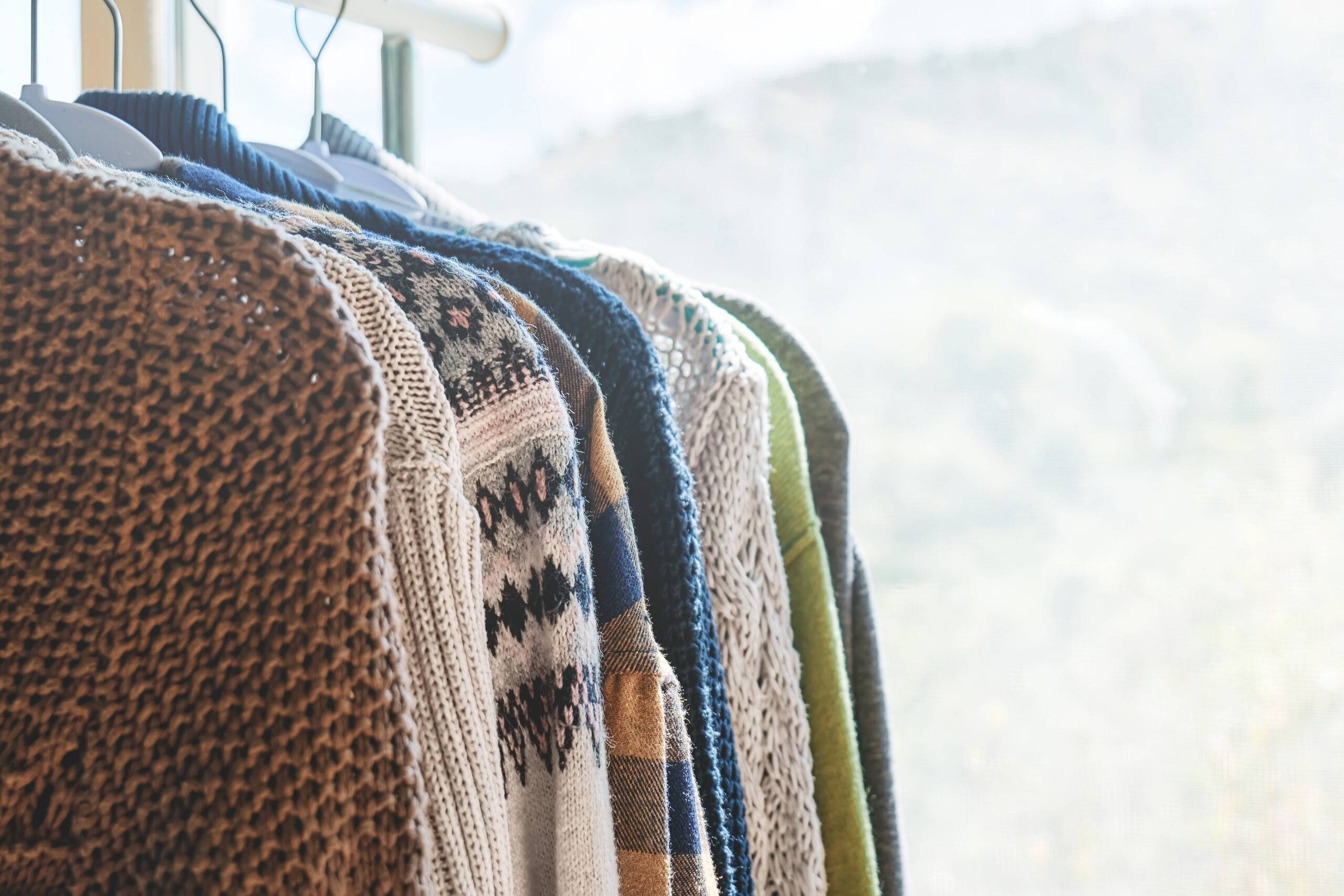 Knitted sweaters on hangers on the clothes rack. Slow Fashion. Conscious consumption. Garage sale, reuse clothes, second hand and eco consumering concept.