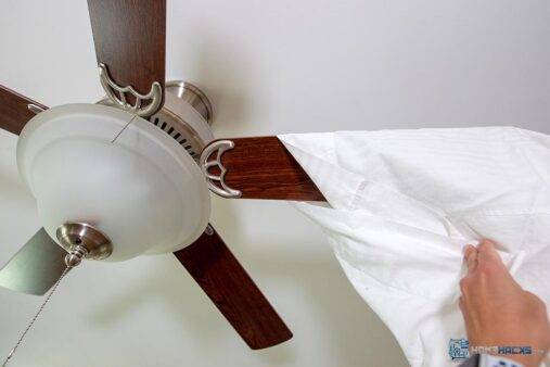 A person putting a pillowcase over the blade of a ceiling fan.