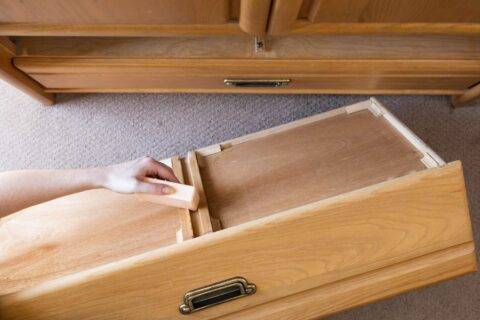 A person rubbing a bar of soap along the bottom of a wooden drawer.