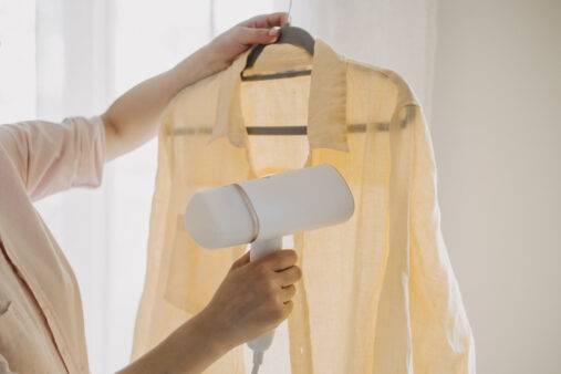 A woman uses a steamer to remove wrinkles from a light yellow shirt, showcasing an effective method for garment care and ironing alternatives.