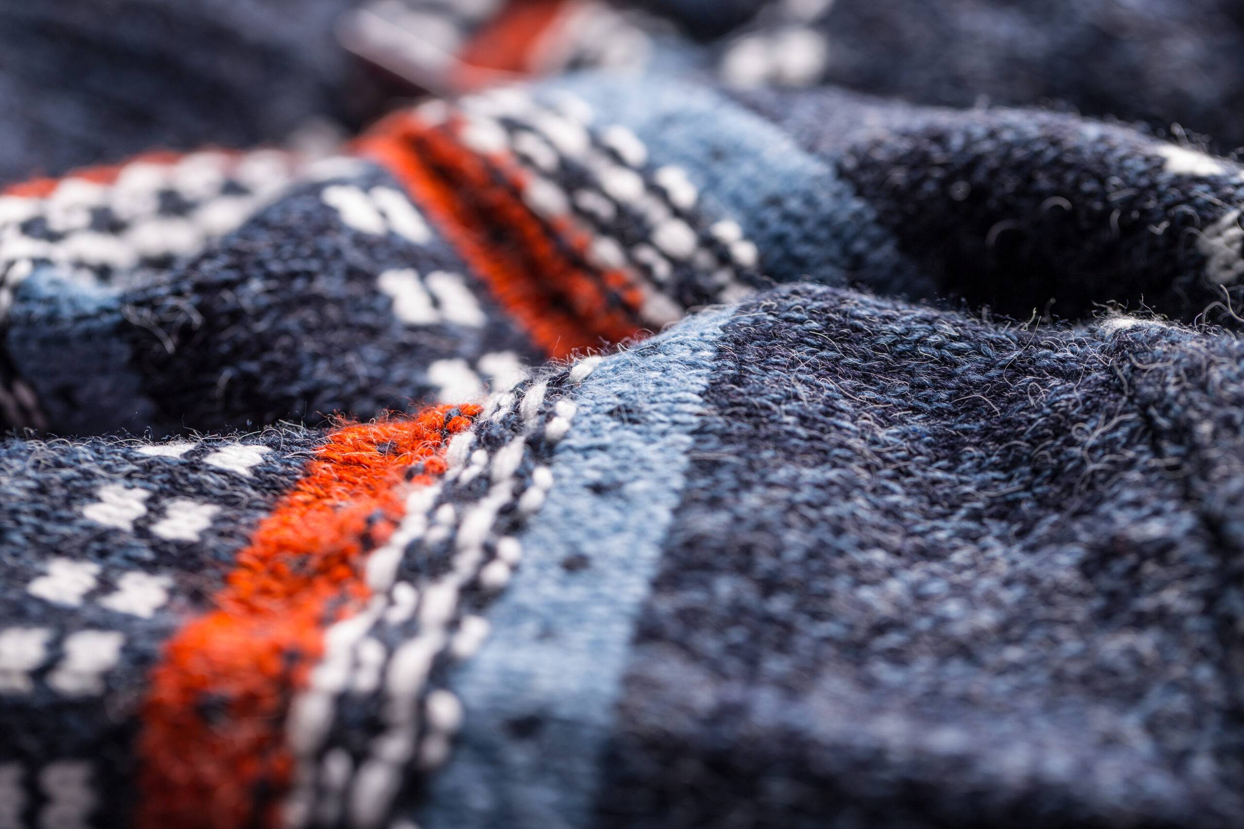 A closeup of a navy blue wool sweater with some orange, white, and light blue patterning.