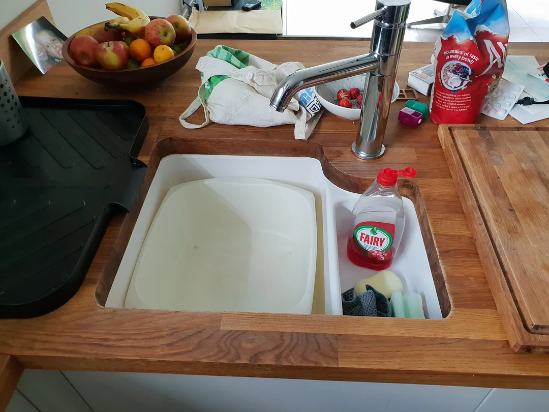 A kitchen sink largely filled with a plastic bin, part of that bin holding dish soap and sponges.