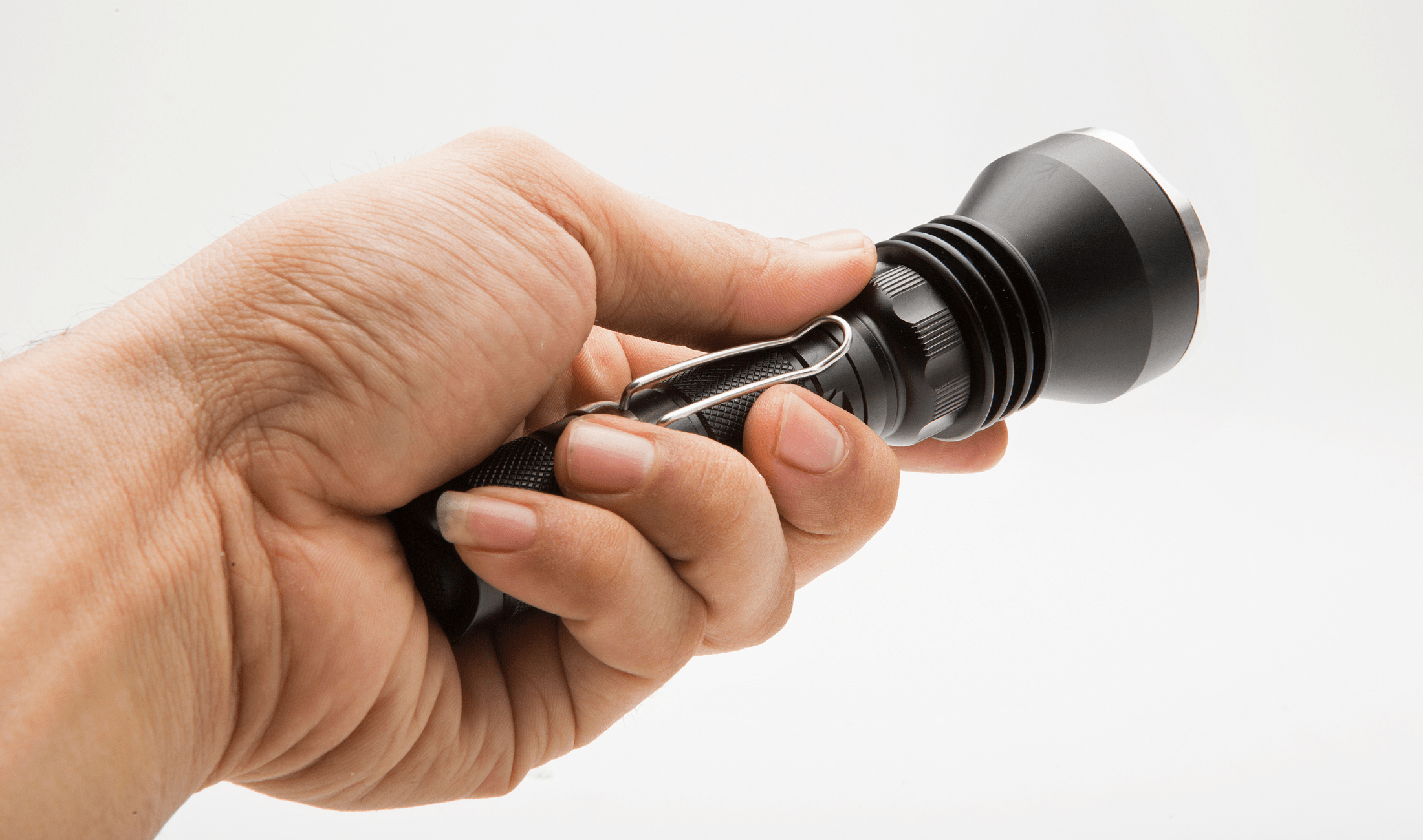 A hand holding a small flashlight against a white background.