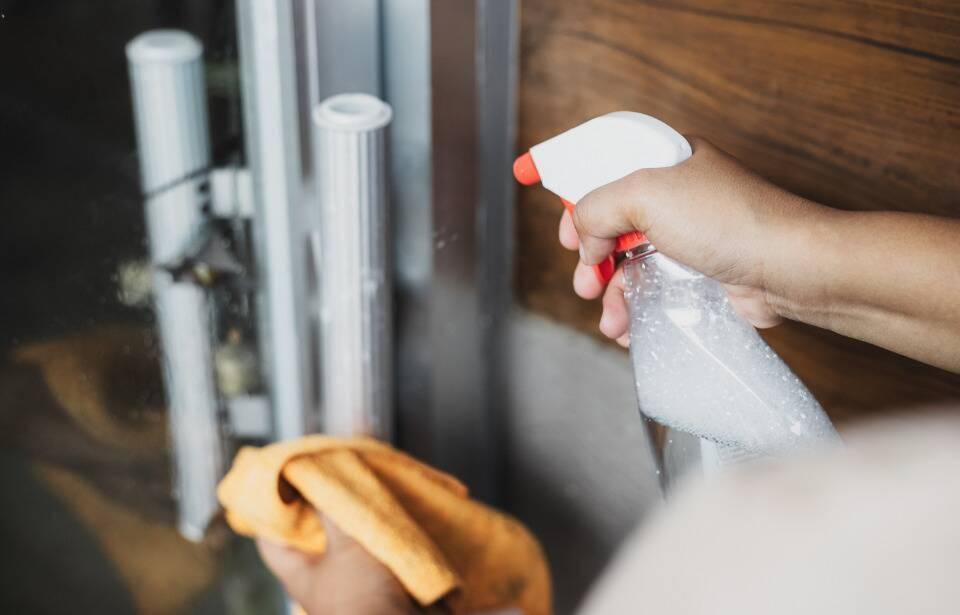A person spraying cleaner on a door handle.