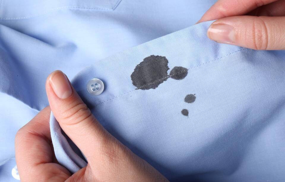 A person holding the hem of a shirt with a black ink stain on it.