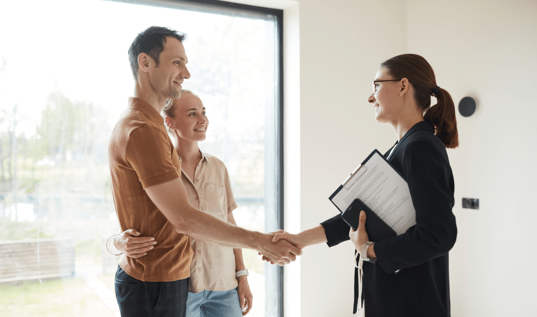 A realtor shaking a man's hand as she stands in front of a couple.