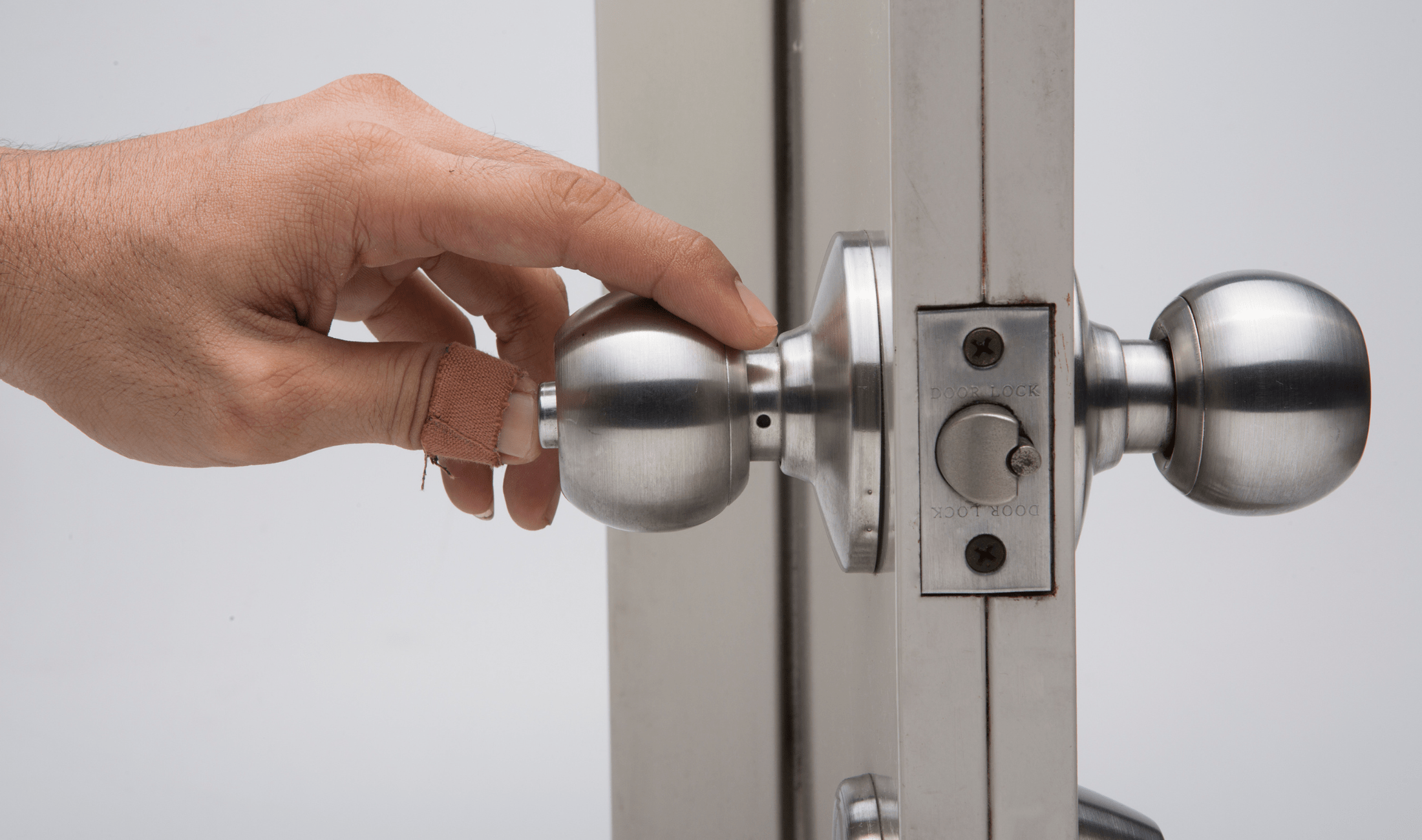 A hand pushing in the button lock on a doorknob