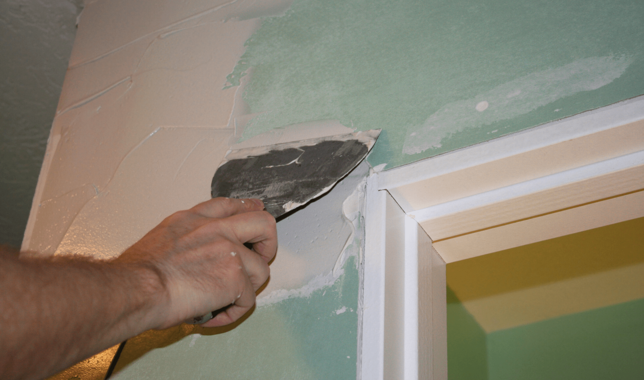 A person using a scraper to spackle a section of drywall.