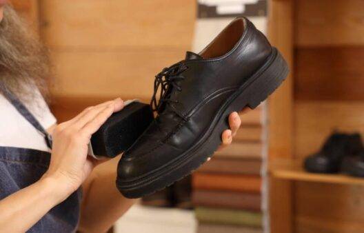 A person polishing a leather shoe with a brush.