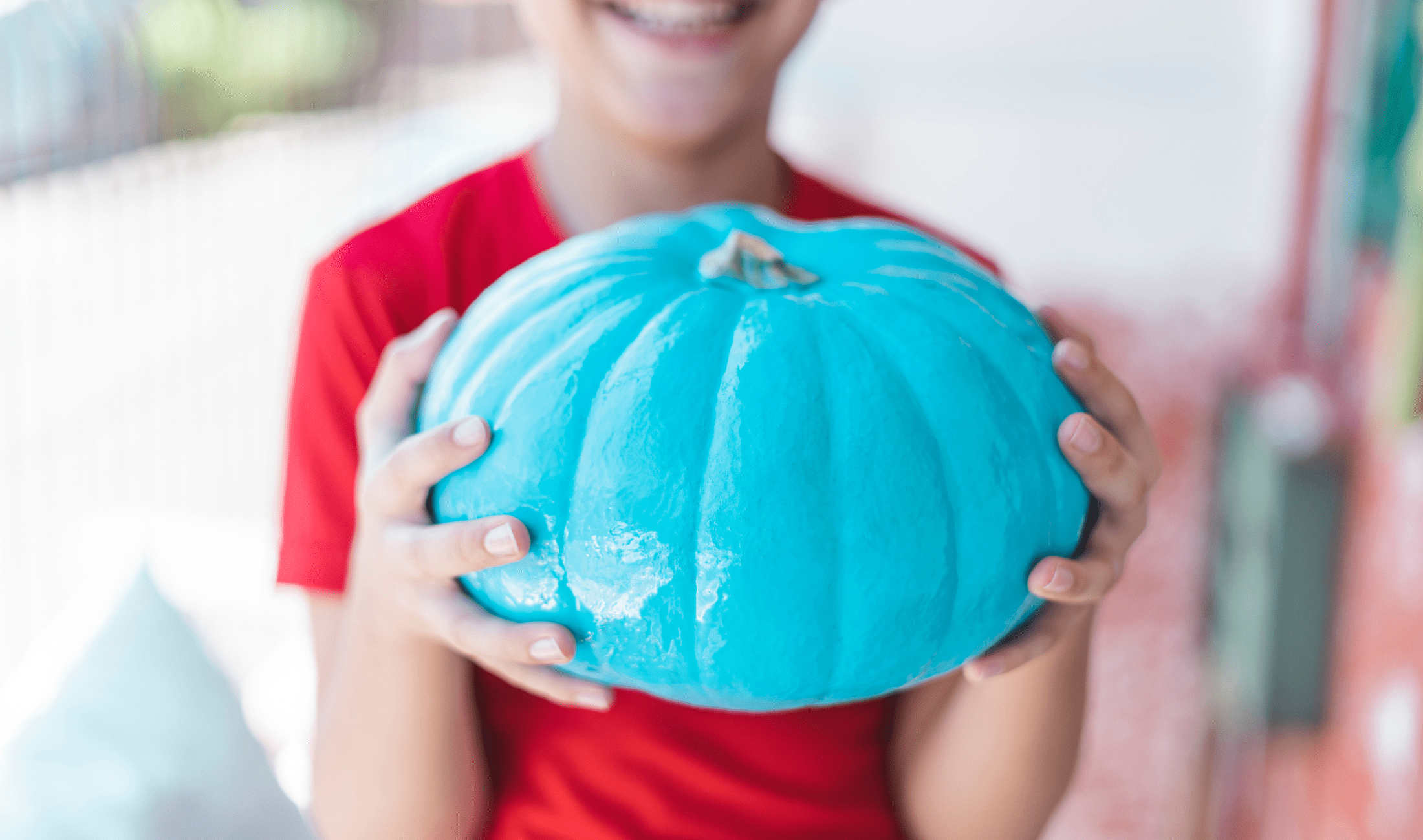 A kid holding a painted blue pumpkin.