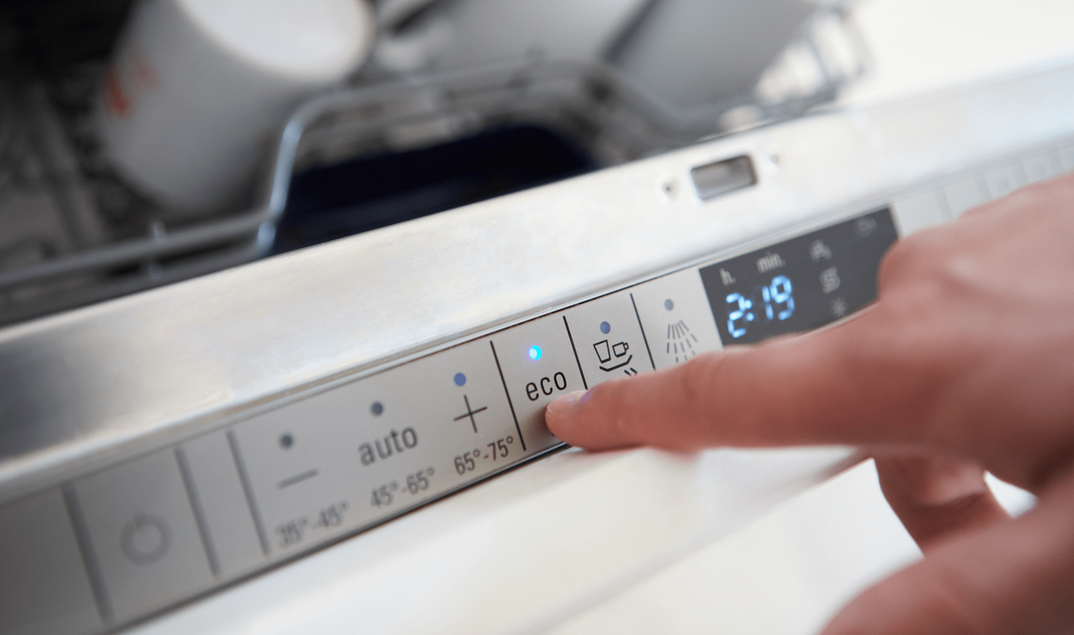 A closeup of a dishwasher's settings with a finger pressing the 'eco' button.
