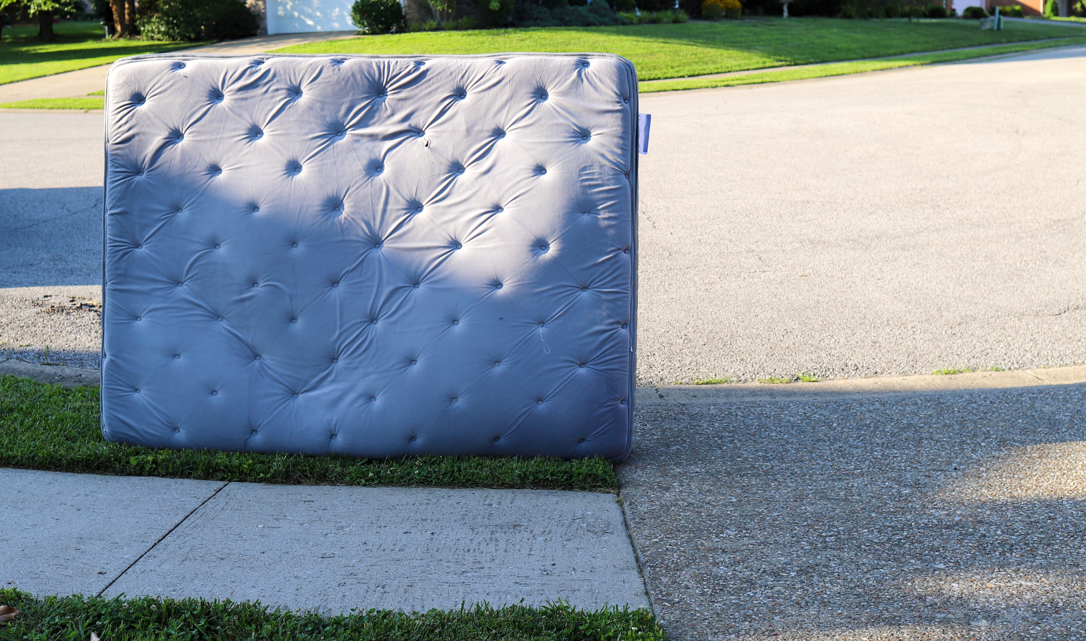 A mattress standing vertically outdoors on someone's curb.