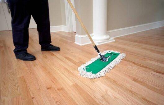 A person using a dusting mop on a wood floor.