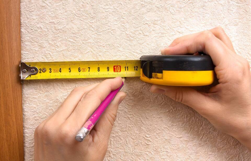Someone marking the wall beneath a tape measure they're holding.