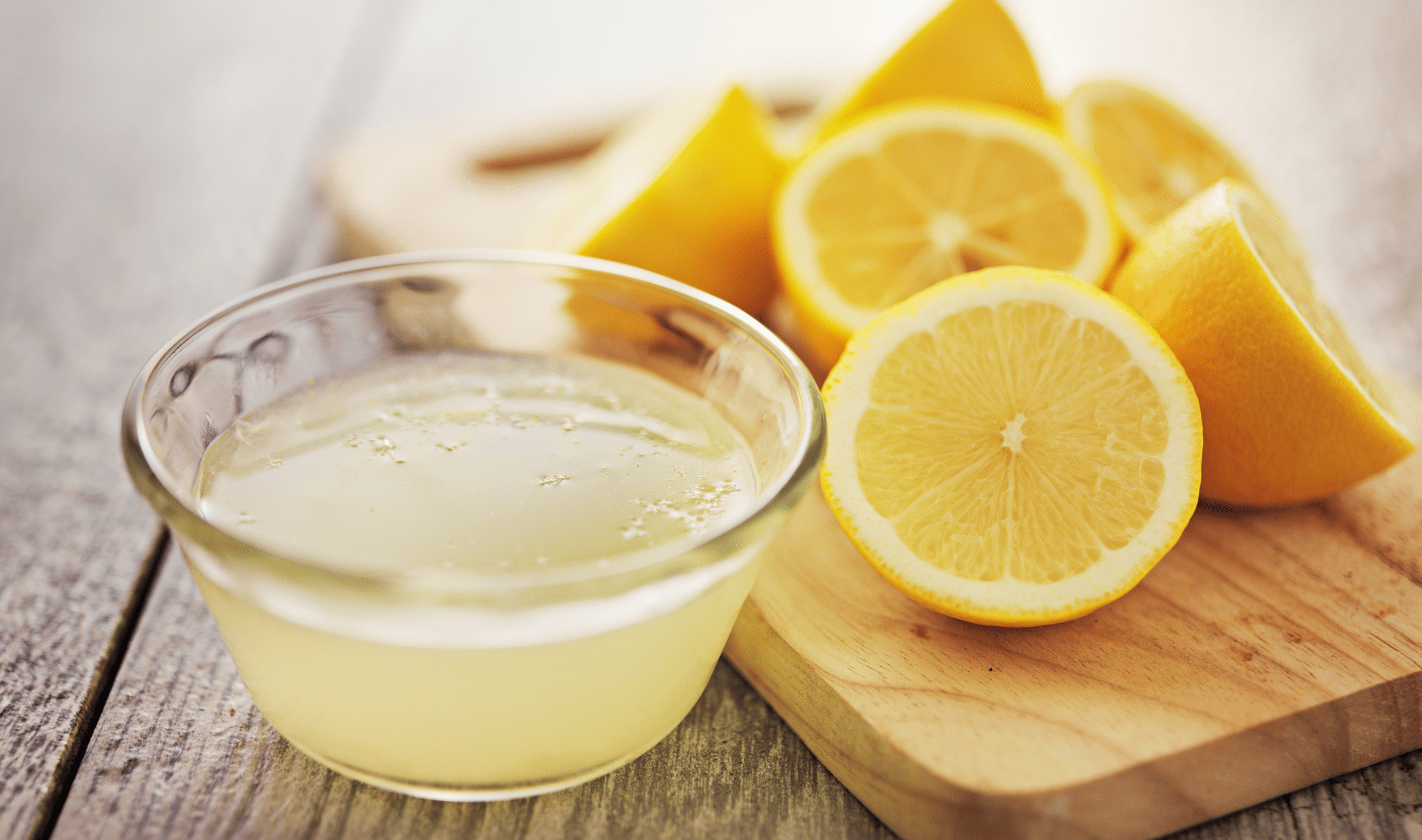 A small bowl of lemon juice next to halved lemons on a cutting board.