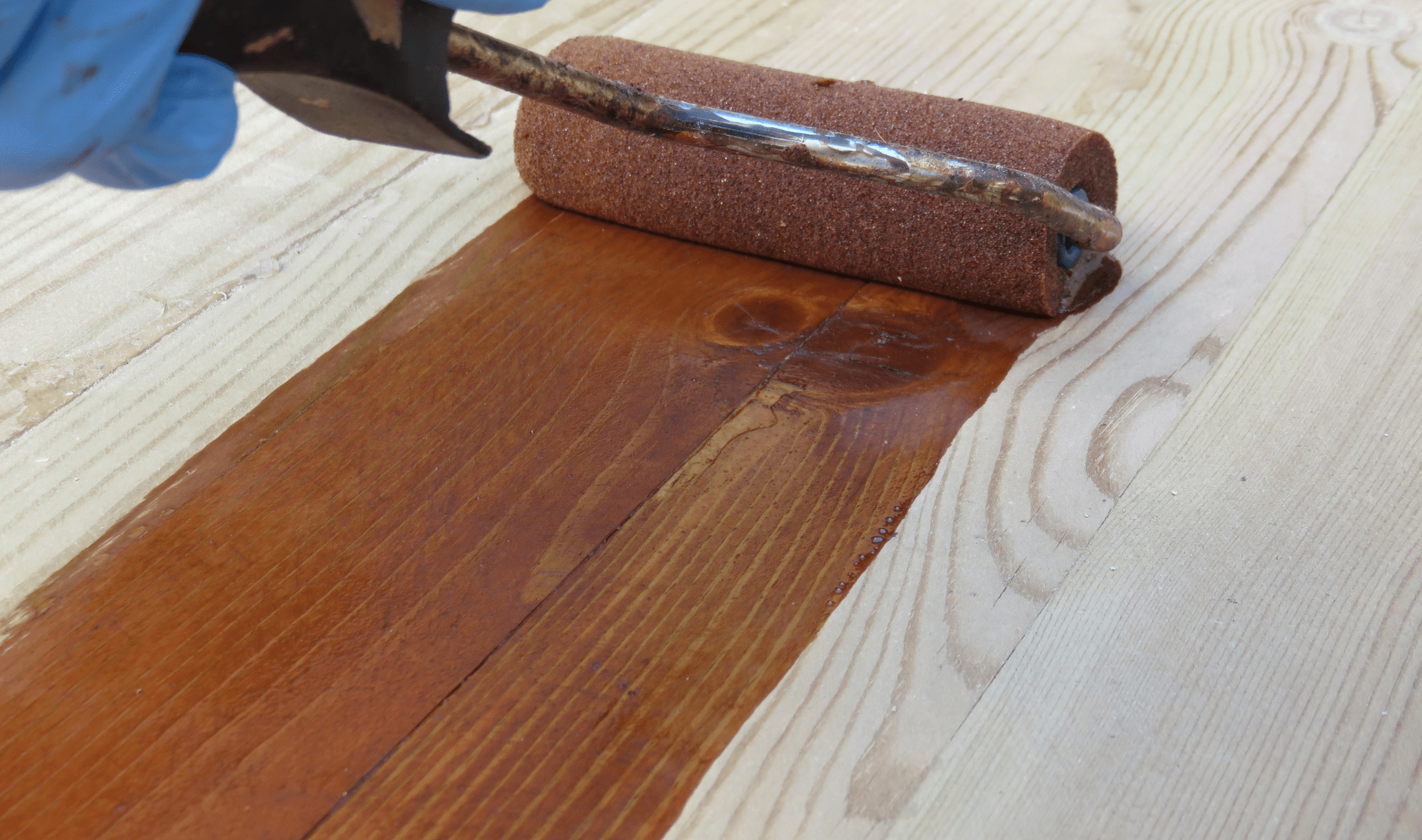 A close photo of someone rolling wood stain onto a bare floor.