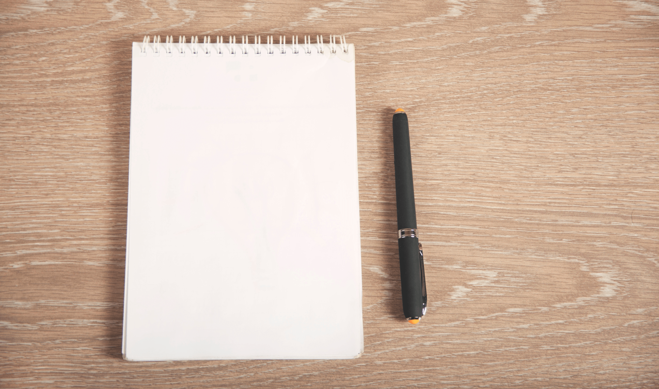 A pen next to a blank notebook on a wooden table.