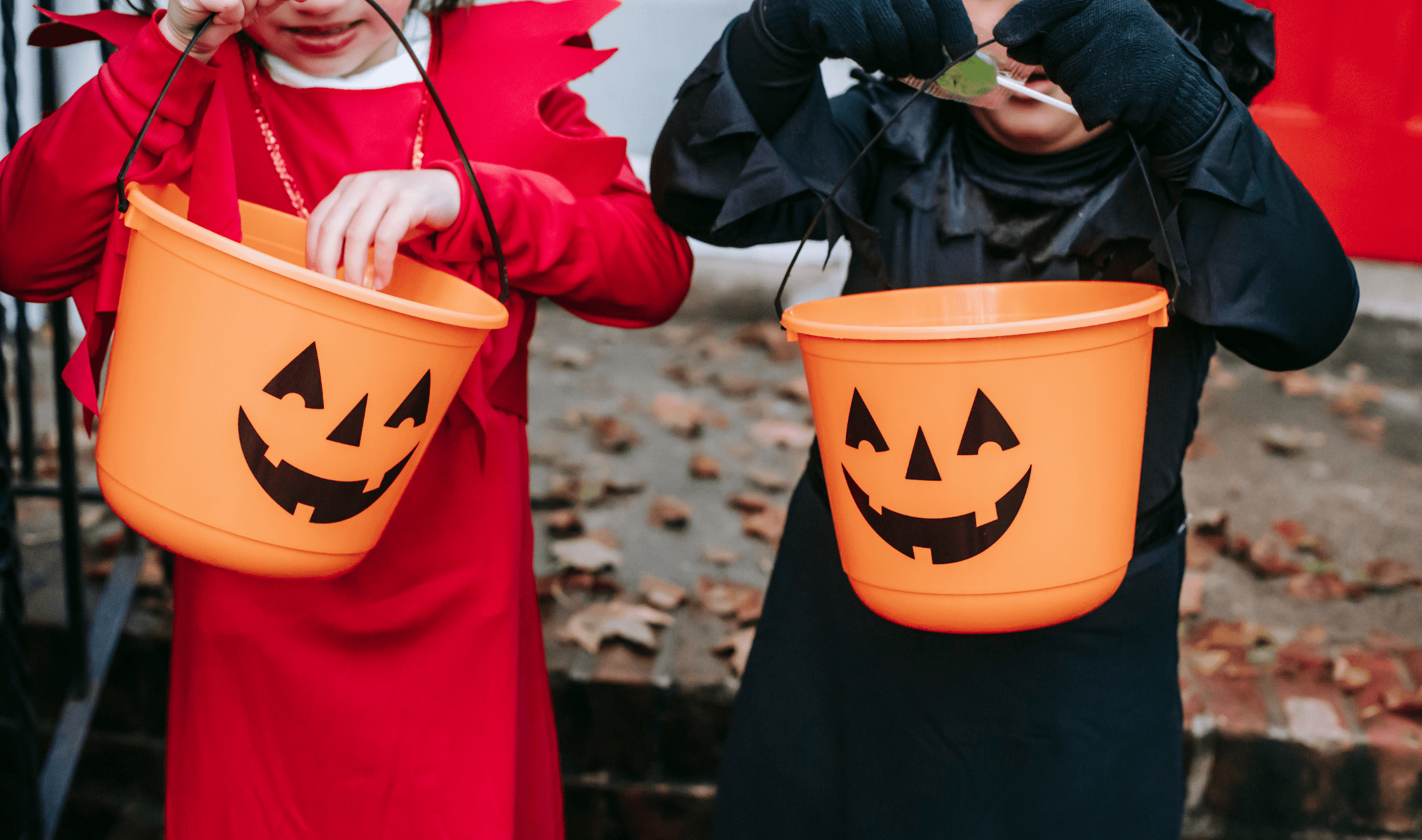 Two children holding halloween jack-o-lantern buckets while wearing Halloween costumes.