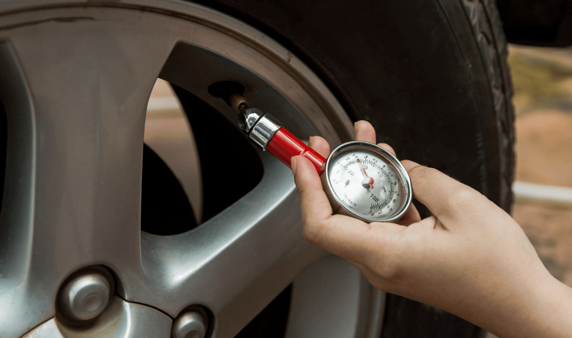 A hand holding and using a tire pressure gauge.