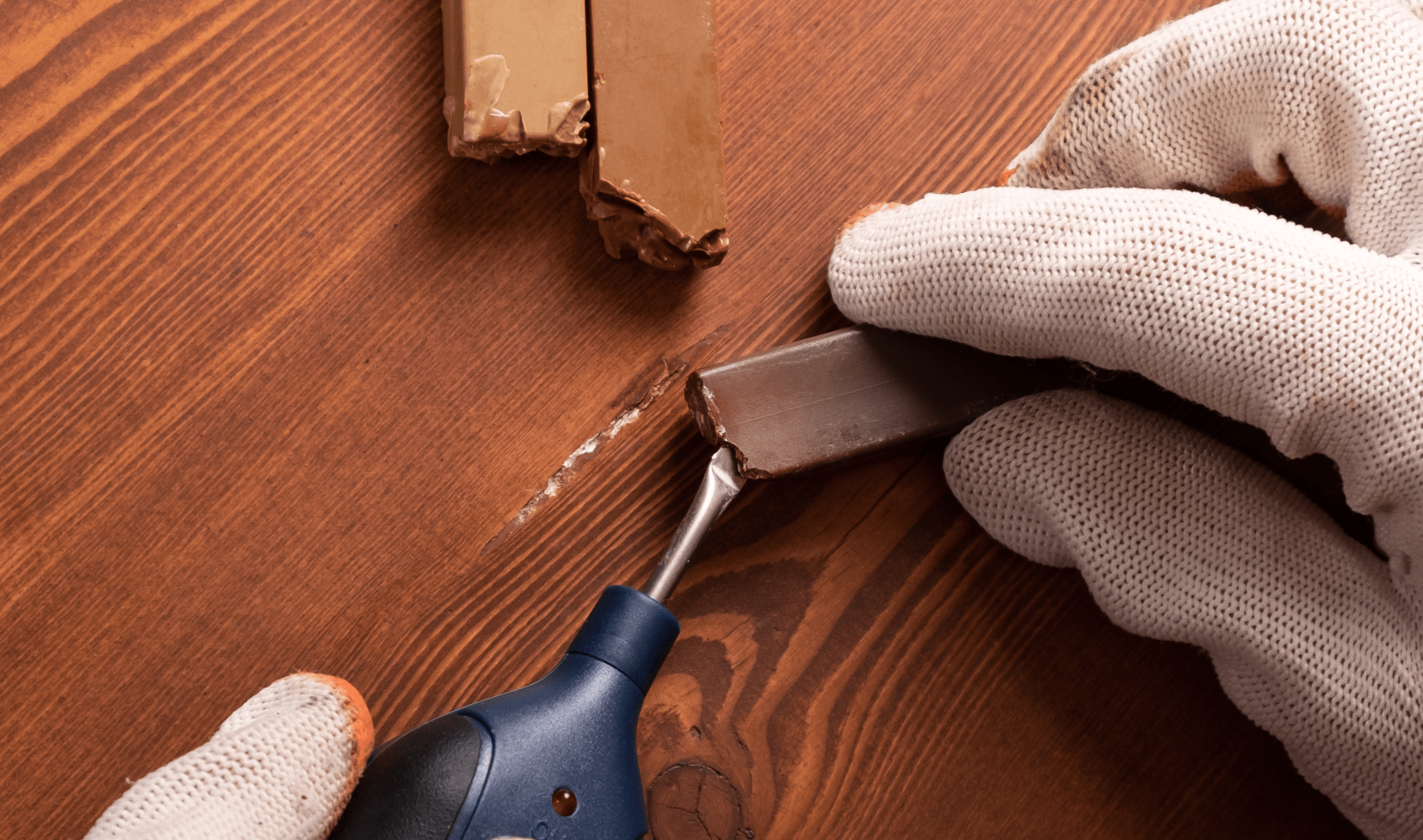 A close photo of someone using wax sticks to repair a wooden floor.
