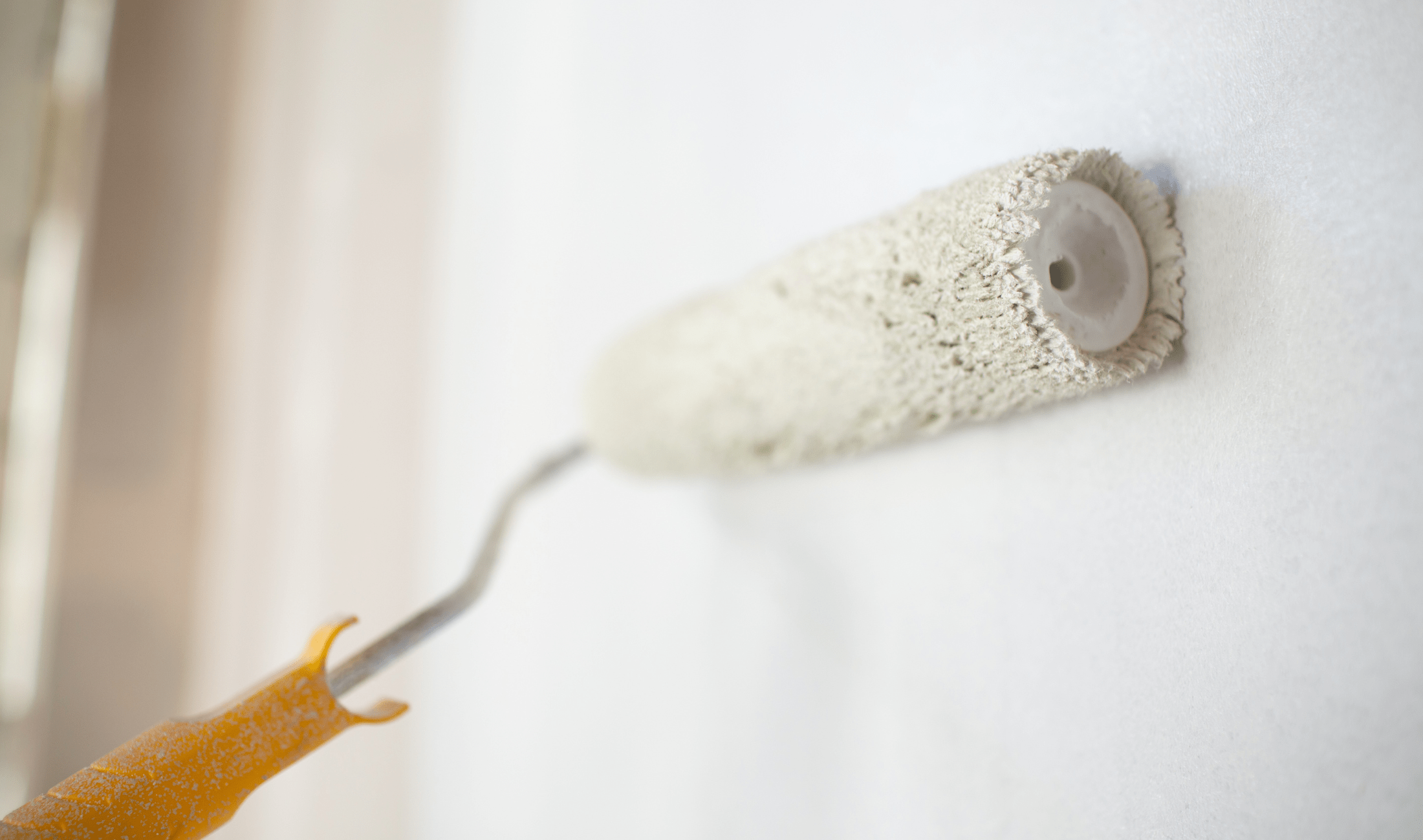 A paint roller painting a wall white.