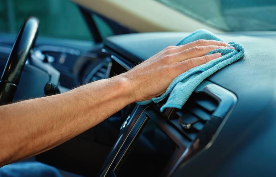 A person wiping downt heir car dashboard with a cloth.