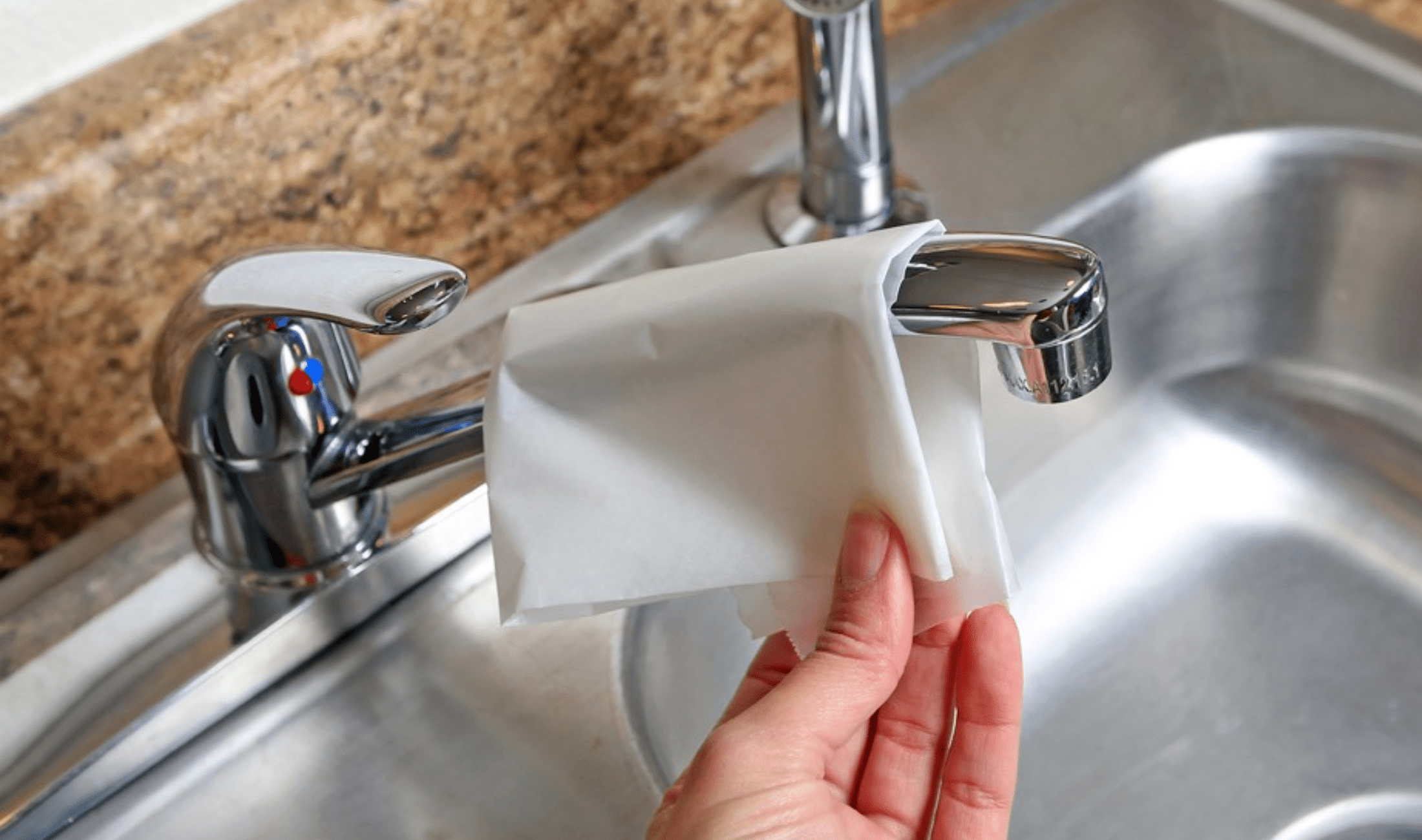 A person using a piece of wax paper to clean a faucet.