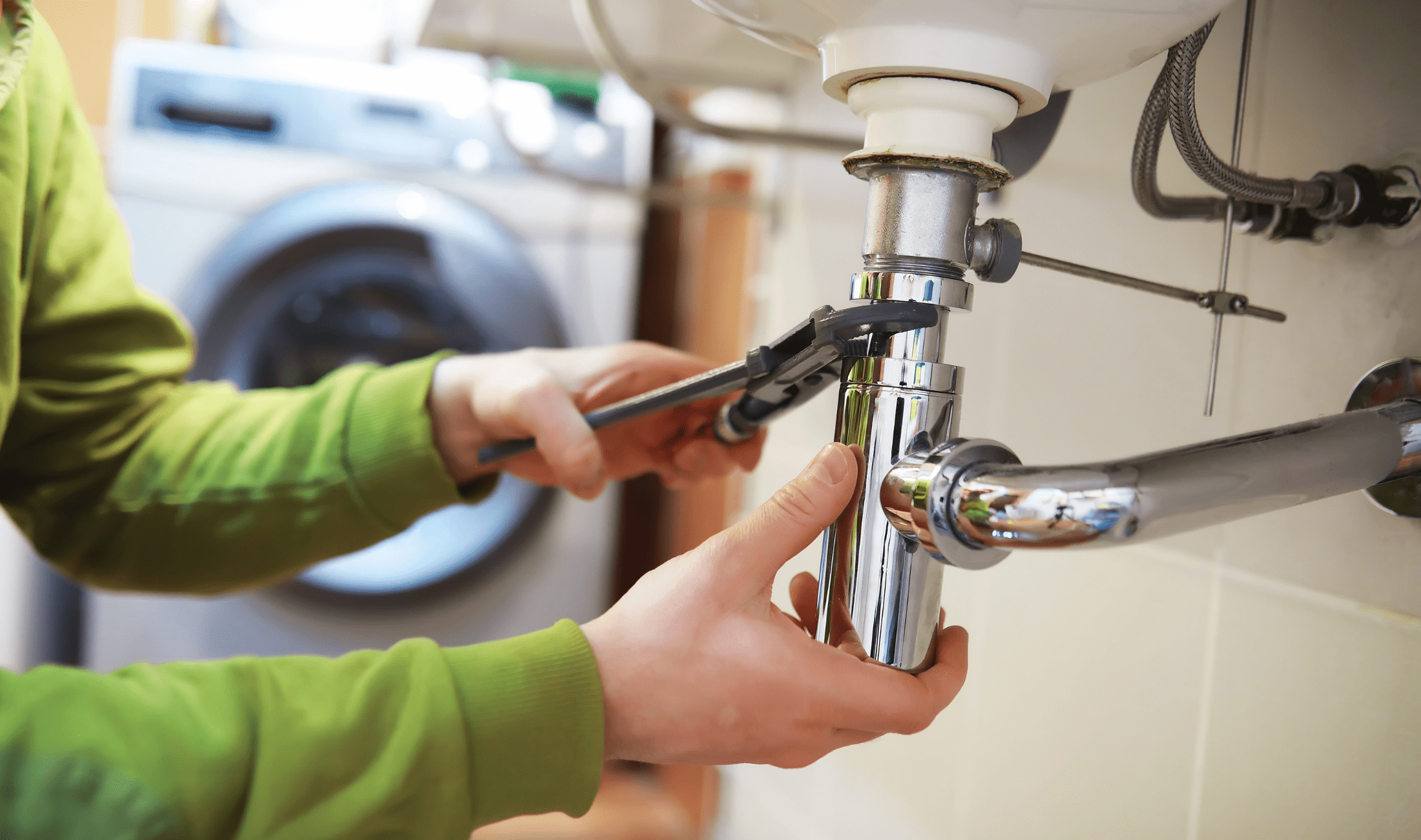 A pair of hands using an adjustable wrench to remove a sink's plumbing.