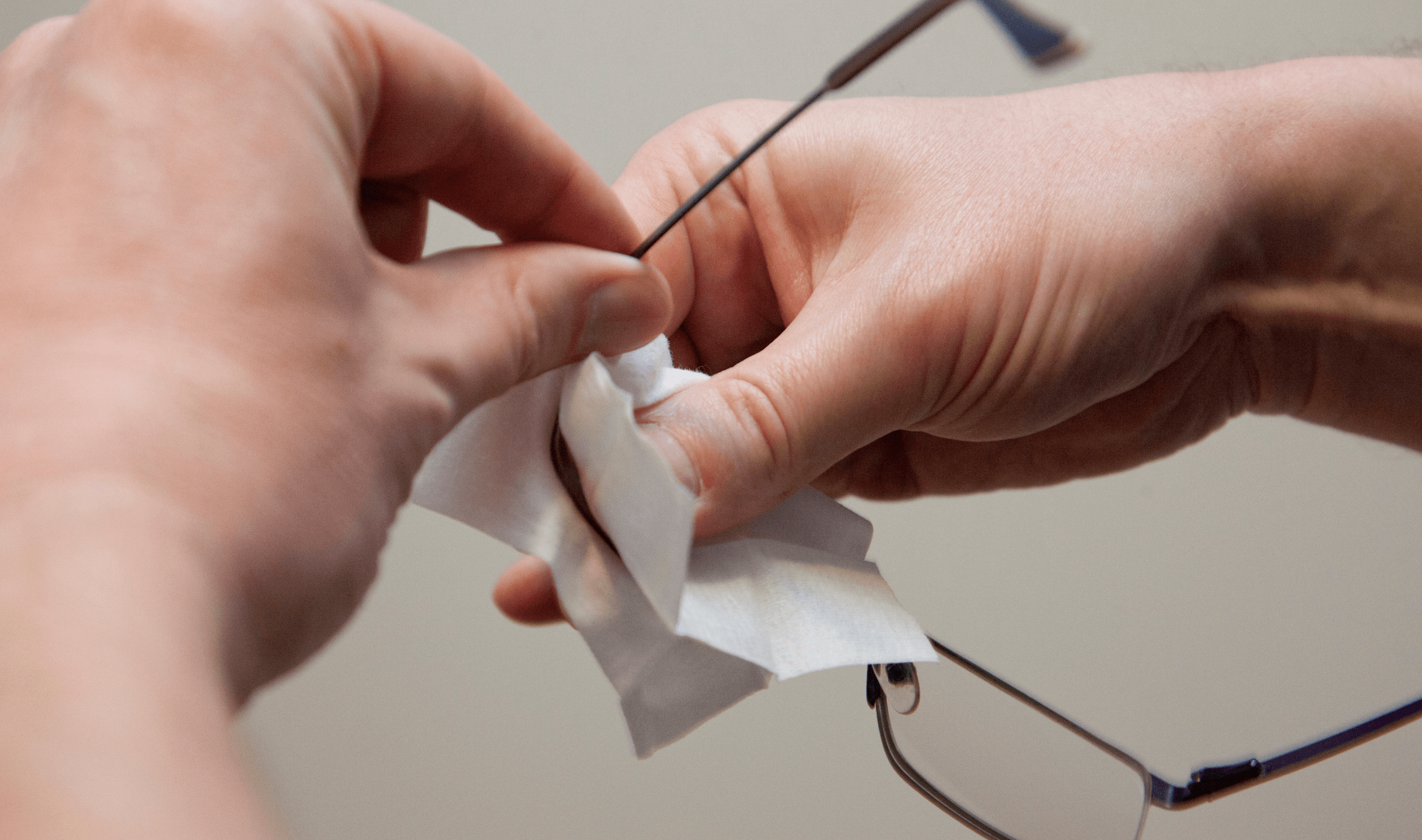 A pair of hands using a disinfectant wipe to clean the lens on a pair of glasses.