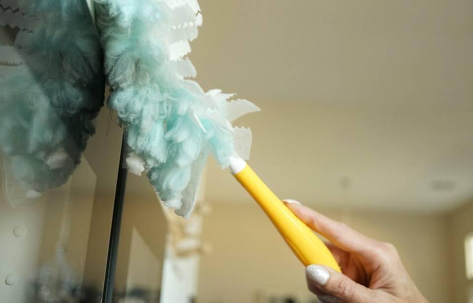A person using a Swiffer duster on a cabinet door.