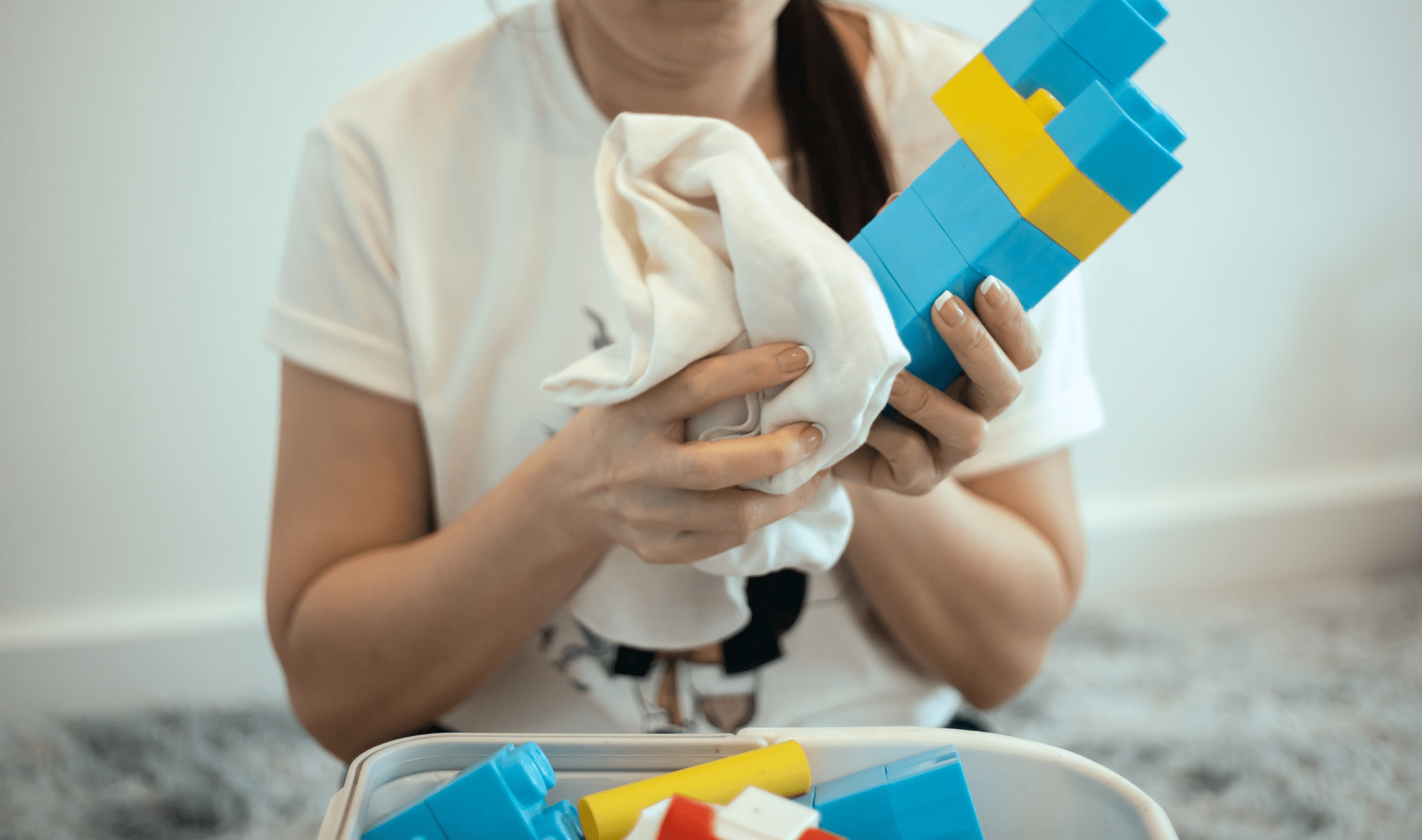 A mother using a disinfectant wipe to clean her child's building blocks.