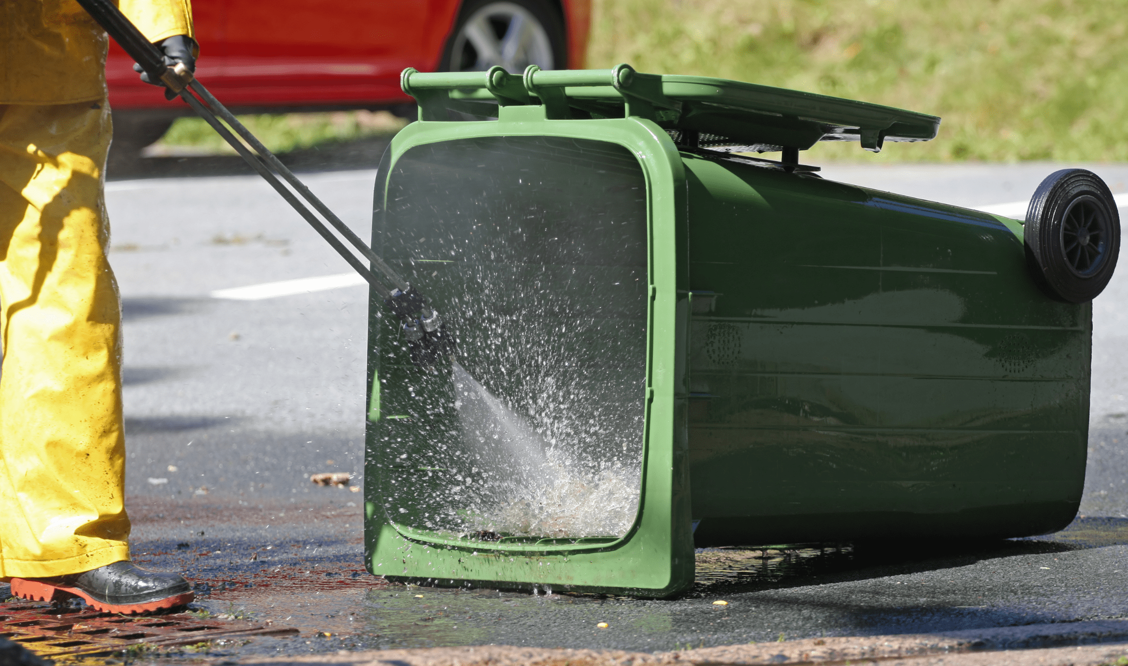 A person power washing a garbage bin.