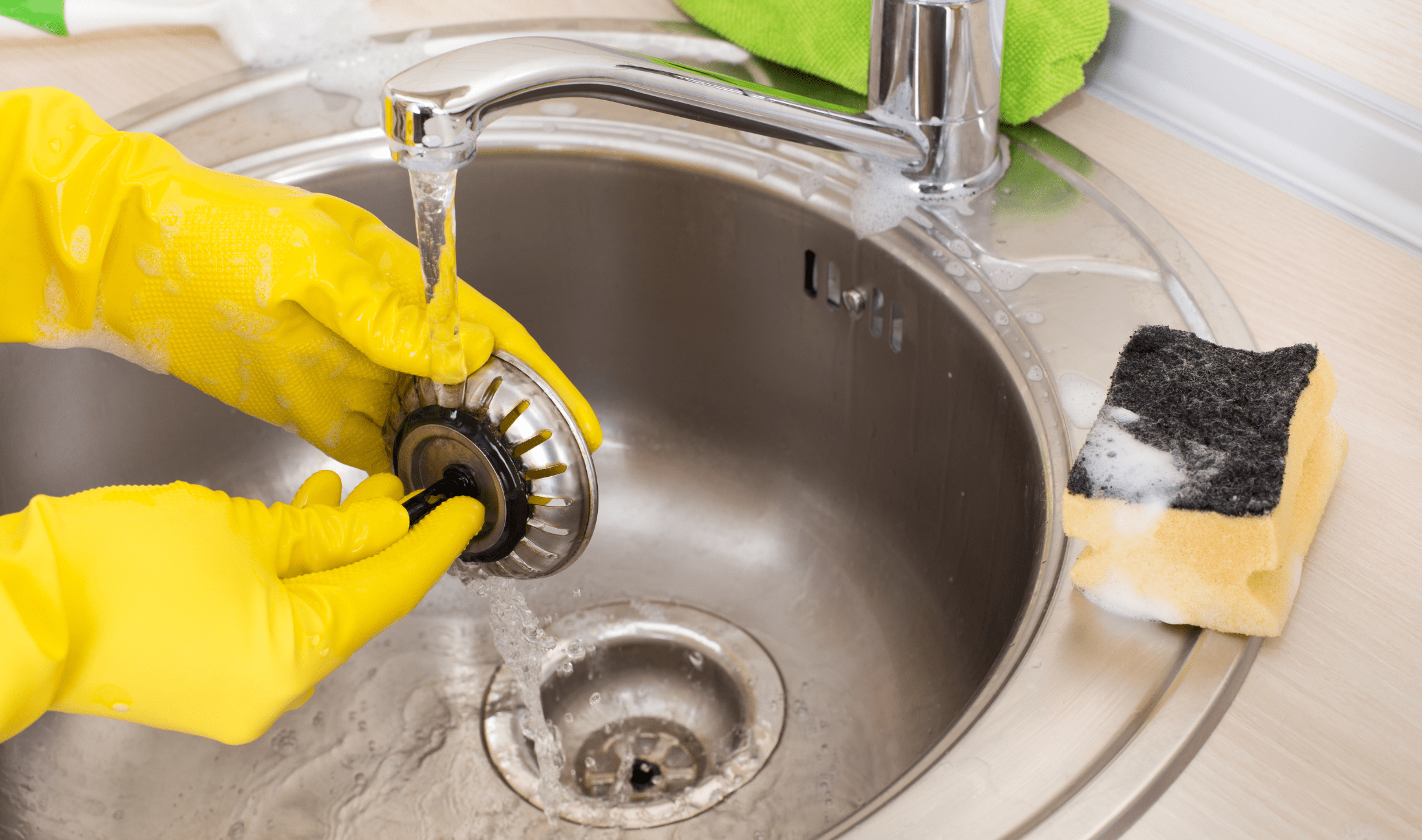 A pair of hands wearing yellow gloves cleaning a sink drain stopper.