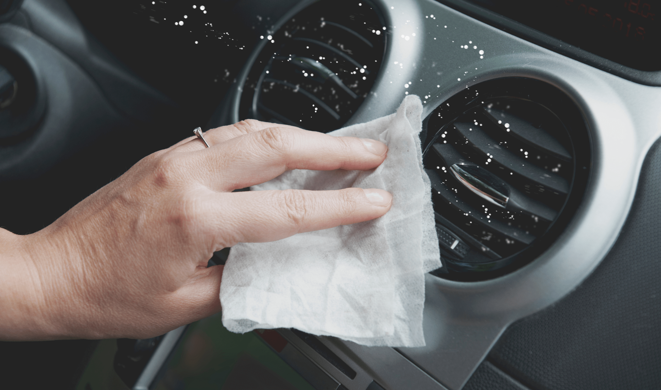 A hand using a disinfectant wipe to wipe down their car's dashboard.