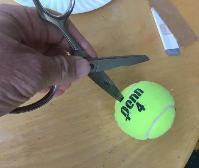 A person poking a pair of scissors into a tennis ball.