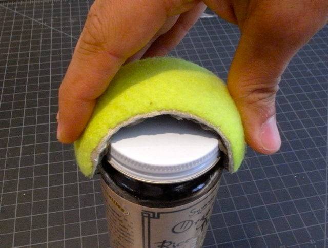 A person's hand holding a curved strip of tennis ball they're using to open a jar.