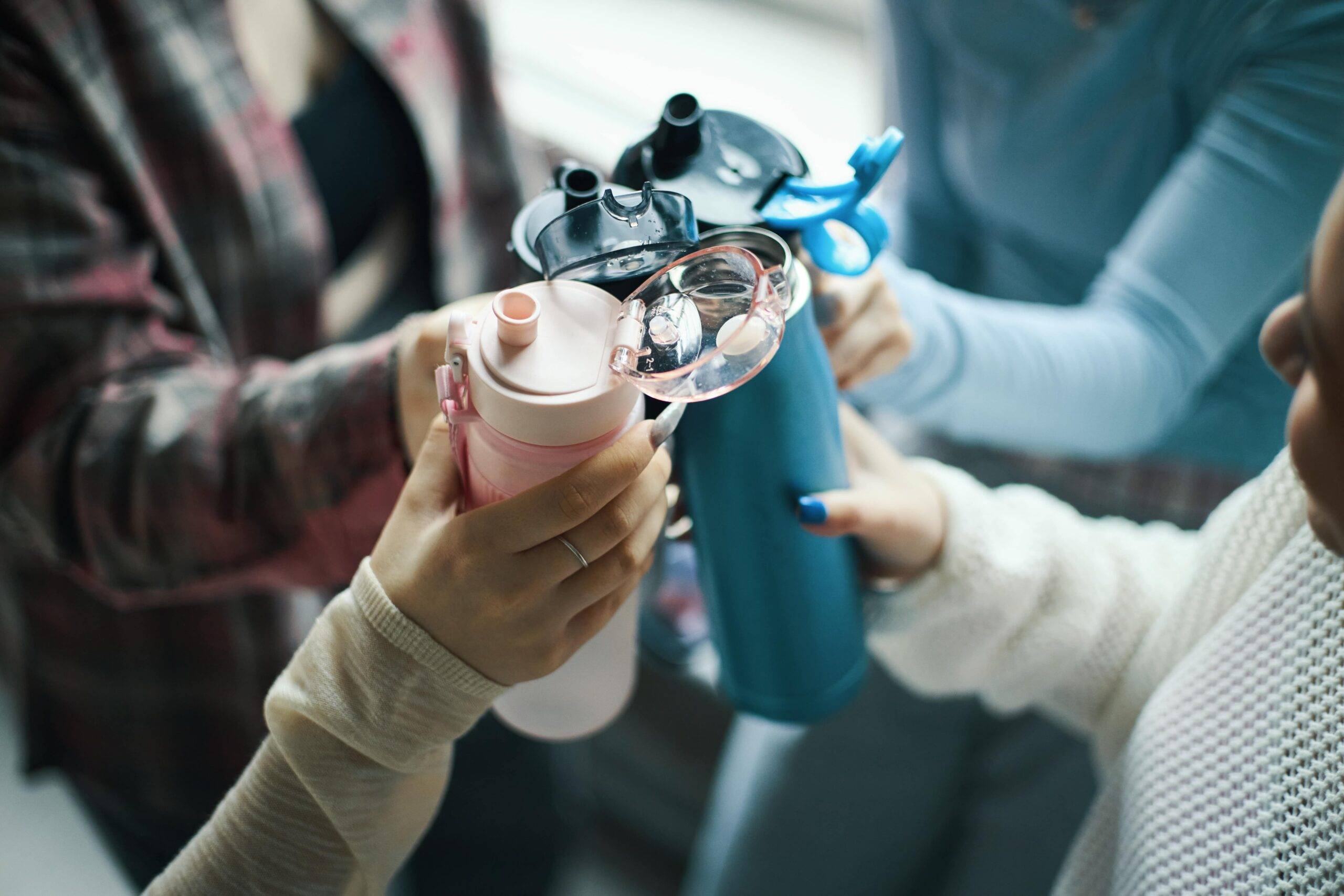 Four friends clinking their reusable water bottles together.