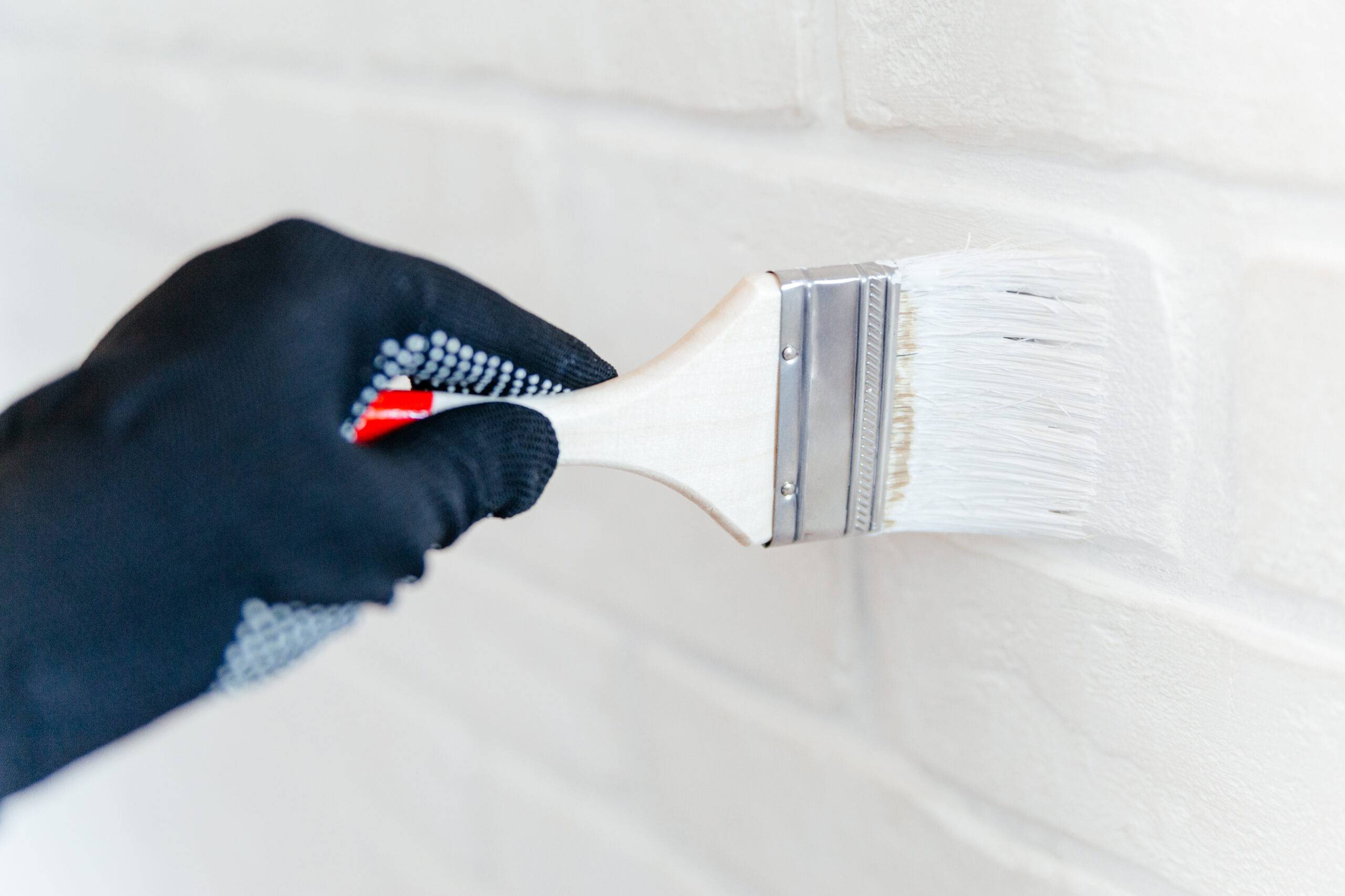 Close-up of a worker's hand with a brush painting a brick wall with white paint. Painting apartment, renovating with white color paint.