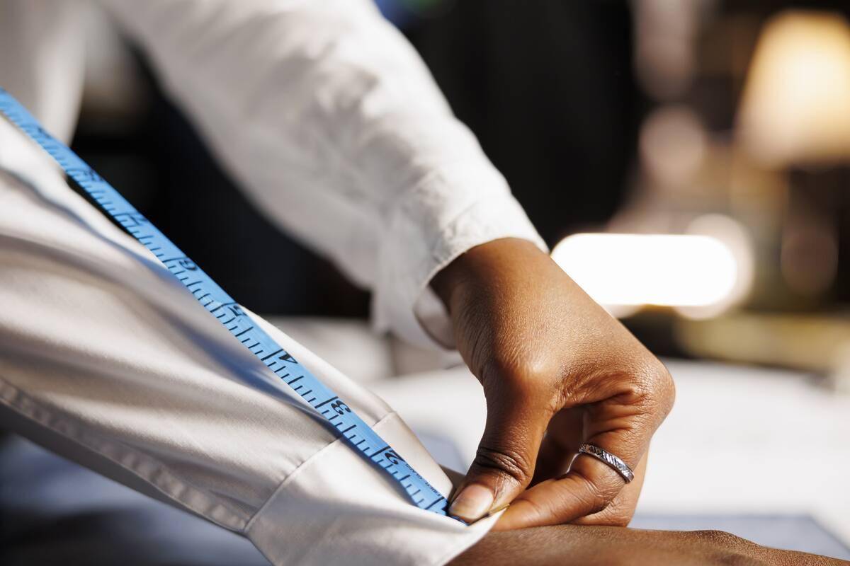 A tailor measuring the arm of a shirt as someone's wearing it.
