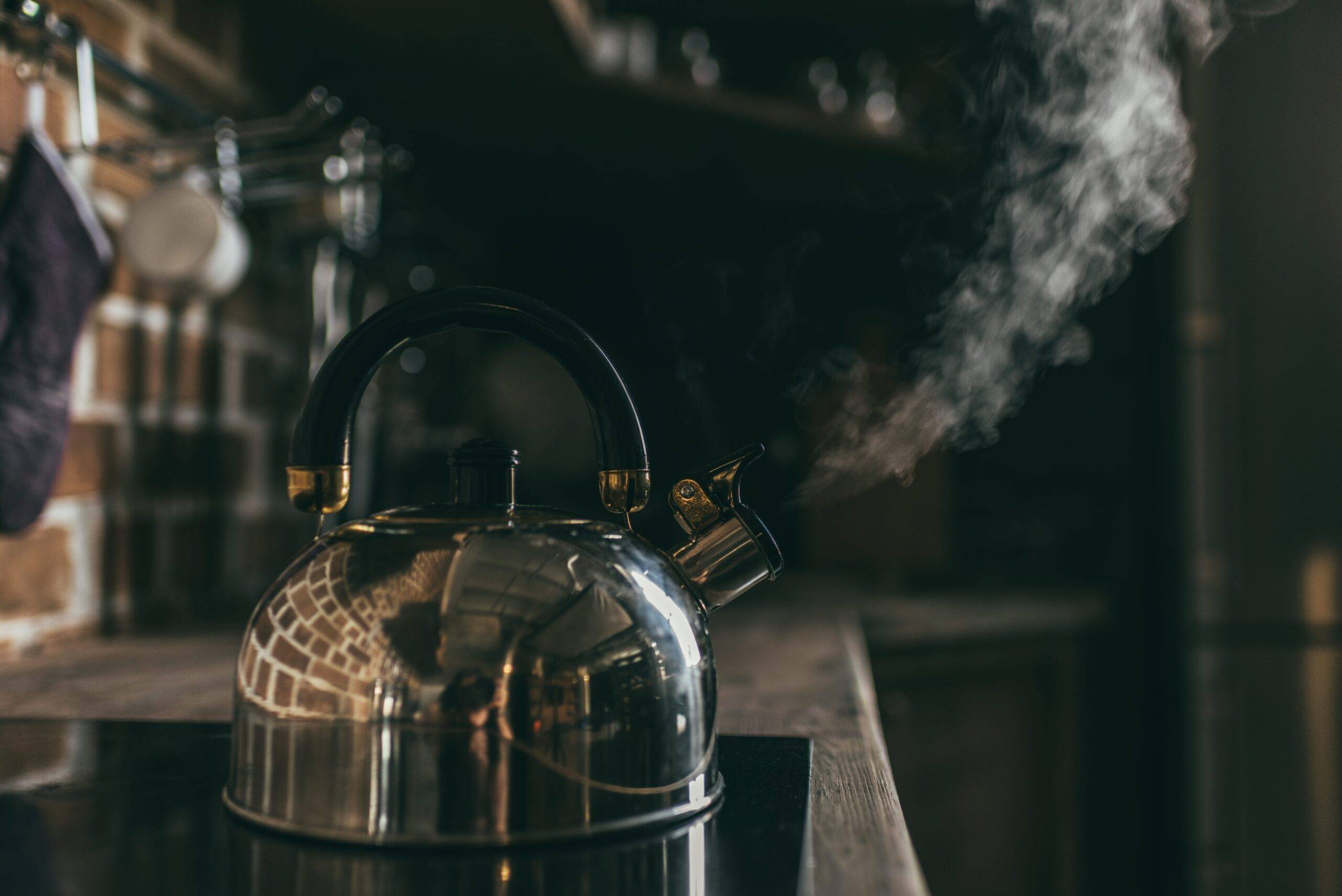 A kettle boiling on a glasstop stove, steam coming out of the neck.