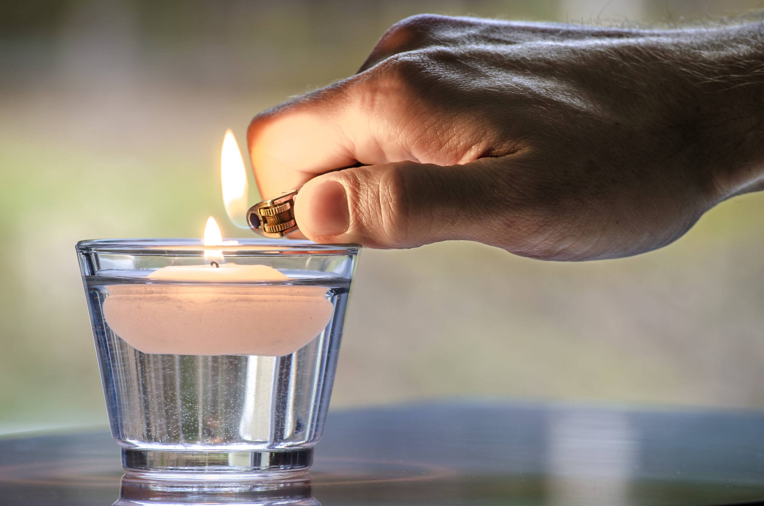Hand with a lighter lighting a candle floating in water.