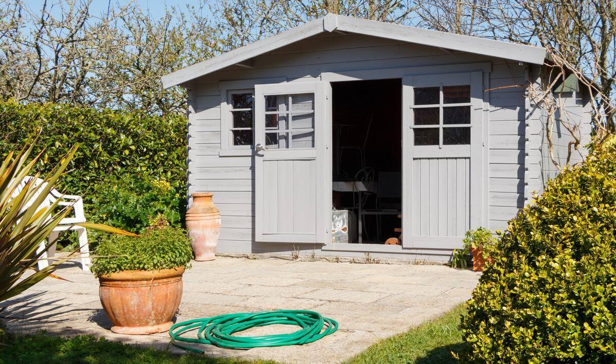 A grey plastic shed in a backyard, a stone landing in front of it.