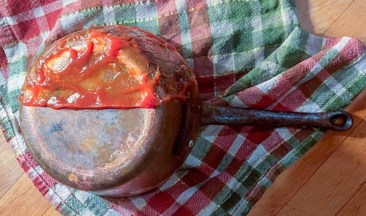 A pot upside down on top of a tea towel, the top half of the pot covered in ketchup.