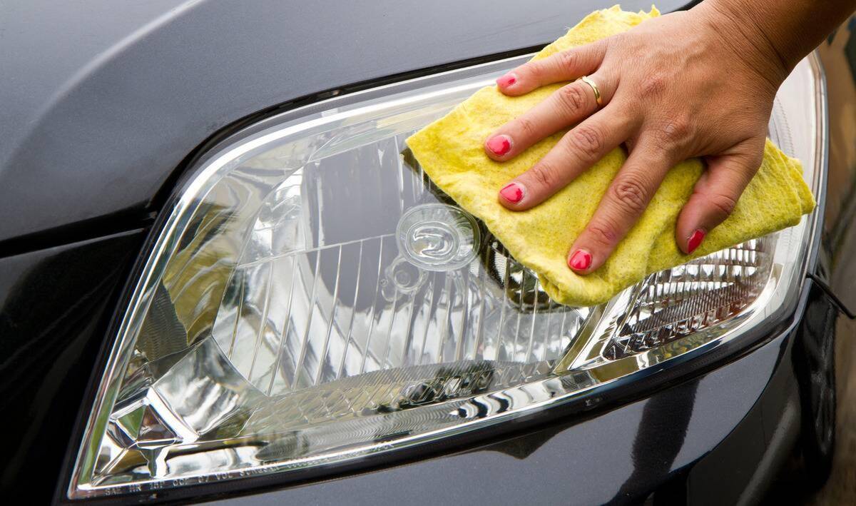 A close photo of a woman's hand using a microfiber cloth to clean a car headlight.
