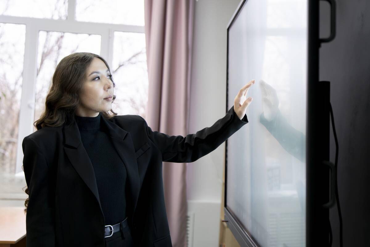 A woman reaching out and barely touching a tv screen.