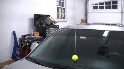 A tennis ball hanging from a string on the roof of a garage, the ball touching a car windshield.