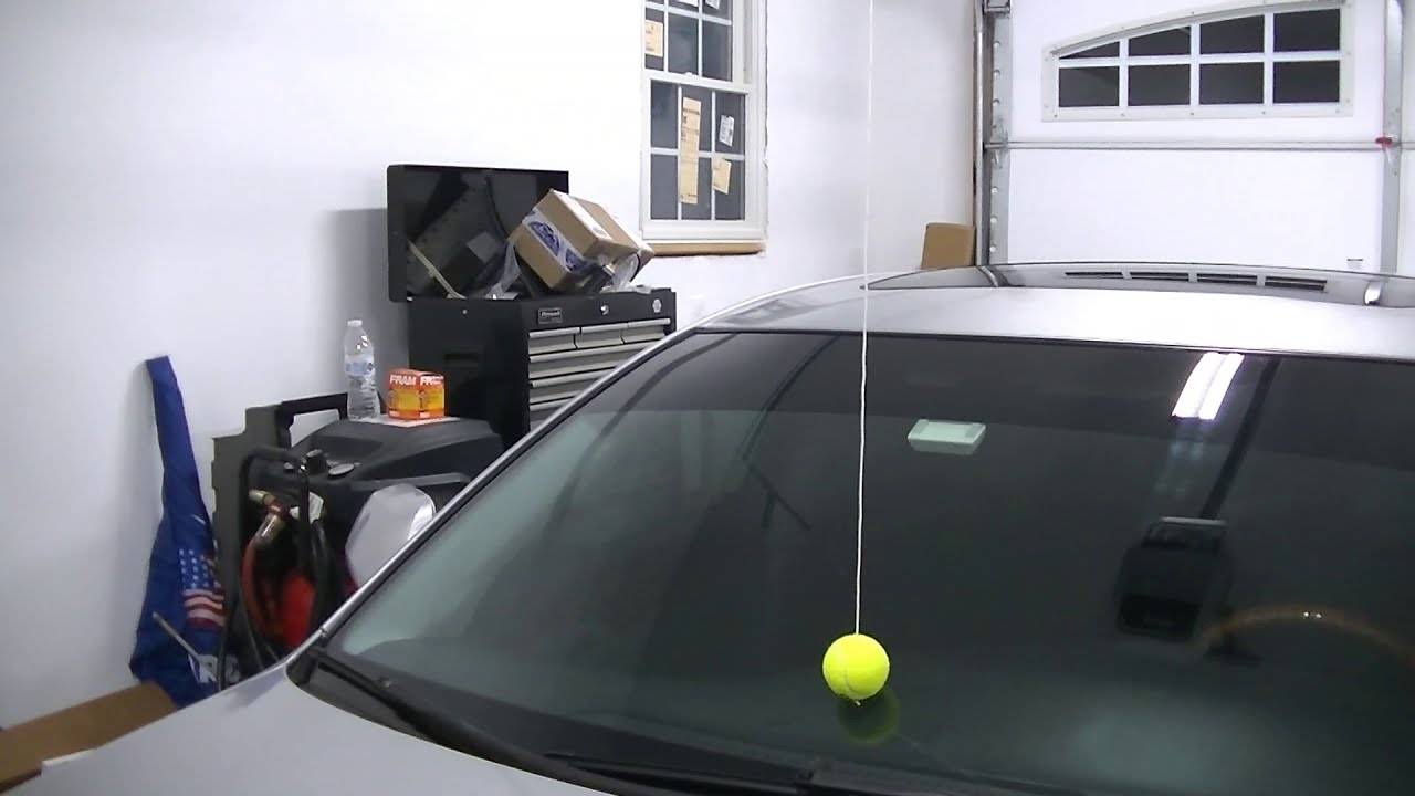 A tennis ball hanging from a string on the roof of a garage, the ball touching a car windshield.